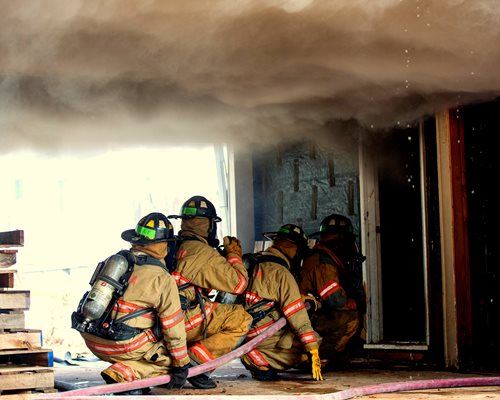 A group of  four firefighters about to enter a burning building with a smoke cloud above them