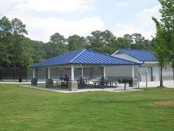The Tumlin Park Pavilion with tables underneath it and trees in the background